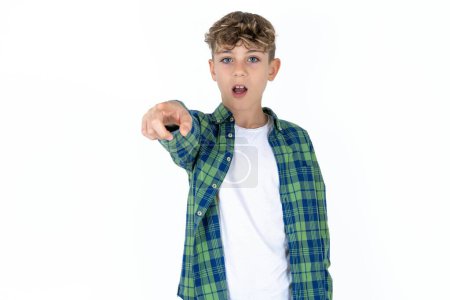 Téléchargez les photos : Beau adolescent garçon portant chemise à carreaux sur fond blanc pointant du doigt surpris devant, bouche ouverte expression étonnée, quelque chose sur le devant. - en image libre de droit