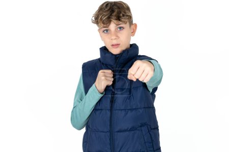 Téléchargez les photos : Beau caucasien adolescent garçon dans bleu gilet poinçonnage poing pour lutter agressif et en colère attaque menace et violence - en image libre de droit