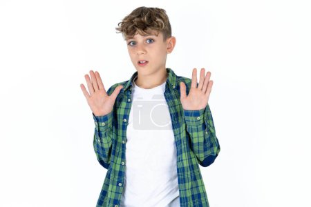 Foto de Guapo adolescente con camisa a cuadros sobre fondo blanco alejando las palmas de las manos mostrando rechazo y negación con miedo y expresión repugnante. Detente y prohibido. - Imagen libre de derechos