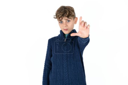 Foto de Hermoso chico adolescente caucásico en suéter azul burlándose de la gente con los dedos en la frente haciendo gesto perdedor burlándose e insultando. - Imagen libre de derechos