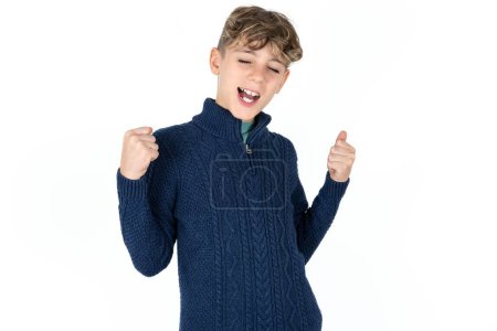 Foto de Extático guapo caucásico adolescente chico en azul suéter gritar fuerte sí puño arriba levantar ganar lotería - Imagen libre de derechos