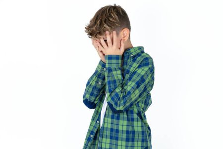 Foto de Triste guapo adolescente chico usando a cuadros camisa sobre blanco fondo llorando cubriendo su cara con sus manos. - Imagen libre de derechos