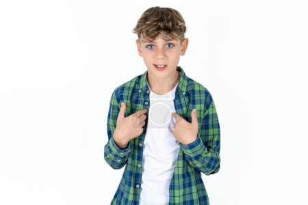 Photo for Embarrassed handsome teen boy wearing plaid shirt over white background indicates at herself with puzzled expression, being shocked to be chosen to participate in competition, hesitates about something - Royalty Free Image