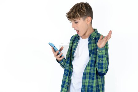 Photo for Angry handsome teen boy wearing plaid shirt over white background screaming on the phone, having an argument with an employee. Troubles at work. - Royalty Free Image