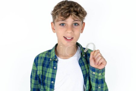 Photo for Handsome teen boy wearing plaid shirt over white background holding an invisible braces aligner, recommending this new treatment. Dental healthcare concept. - Royalty Free Image