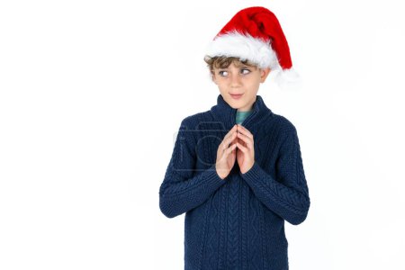 Photo for Handsome caucasian teen boy in blue sweater and christmas hat steepled fingers and looks mysterious aside has great evil plan in mind - Royalty Free Image
