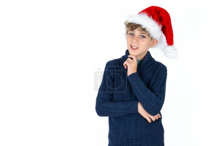 Photo for Handsome caucasian teen boy in blue sweater and christmas hat laughs happily keeps hand on chin expresses positive emotions smiles broadly has carefree expression - Royalty Free Image