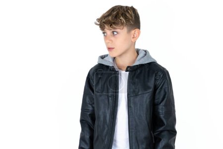 Photo for Handsome teen boy in leather jacket posing over white studio background stares aside with wondered expression has speechless expression. Embarrassed model looks in surprise - Royalty Free Image