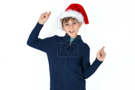 Téléchargez les photos : Photo de beau garçon adolescent caucasien optimiste en pull bleu et chapeau de Noël a du plaisir et danse vêtements insouciants être d'humeur parfaite fait des mouvements. Passe du temps libre sur disco partie - en image libre de droit