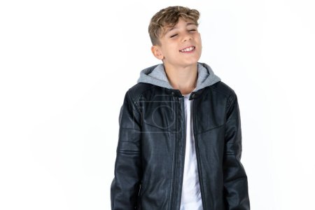 Photo for Positive handsome teen boy in leather jacket posing over white studio background with overjoyed expression closes eyes and laughs shows white perfect teeth - Royalty Free Image