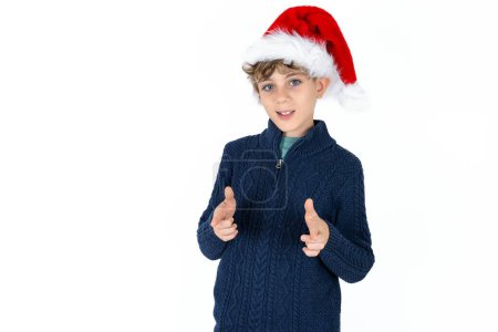 Téléchargez les photos : Beau garçon adolescent caucasien en pull bleu et chapeau de Noël dirige doigts à la caméra sélectionne quelqu'un. Je vous recommande. Meilleur choix - en image libre de droit