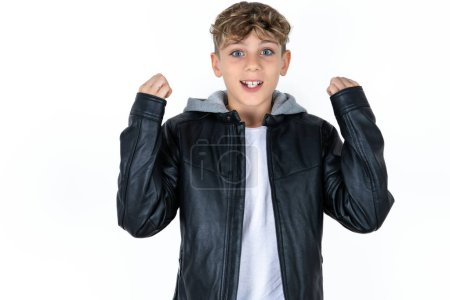 Photo for Shocked ecstatic handsome teen boy in leather jacket posing over white studio background win luck lottery raise hands up shout yea - Royalty Free Image