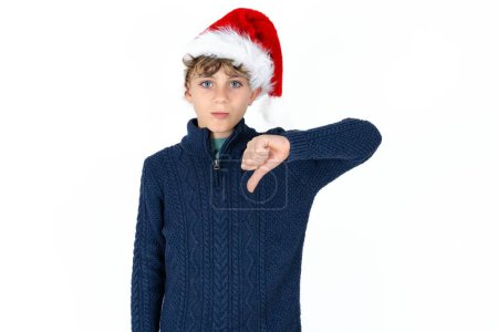 Foto de Guapo caucásico adolescente chico en azul suéter y sombrero de Navidad buscando infeliz y enojado mostrando rechazo y negativo con los pulgares hacia abajo gesto. Mala expresión. - Imagen libre de derechos