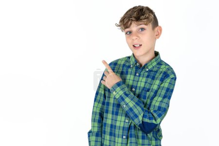 Téléchargez les photos : Beau adolescent garçon portant plaid chemise sur fond blanc heureux gai démontrer copie espace regarder nouveauté - en image libre de droit