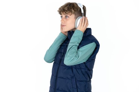 Photo for Handsome Caucasian teen boy in blue vest wears stereo headphones listens music concentrated aside. People hobby lifestyle concept - Royalty Free Image