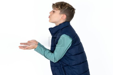 Téléchargez les photos : Profil vue de côté, portrait de beau garçon adolescent caucasien en gilet bleu envoyant baiser d'air - en image libre de droit