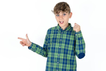 Foto de Guapo adolescente chico usando camisa a cuadros sobre blanco fondo puntos en el espacio vacío sosteniendo puño hacia arriba, gesto ganador. - Imagen libre de derechos