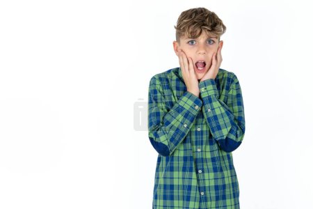 Téléchargez les photos : Bouleversé beau adolescent garçon portant plaid chemise sur fond blanc toucher visage avec deux mains - en image libre de droit
