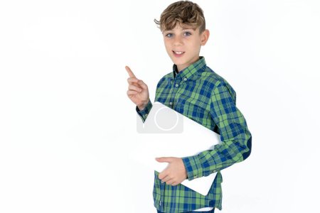 Foto de Guapo adolescente chico usando camisa a cuadros sobre fondo blanco sosteniendo portátil mostrando copia espacio vacío anuncio - Imagen libre de derechos