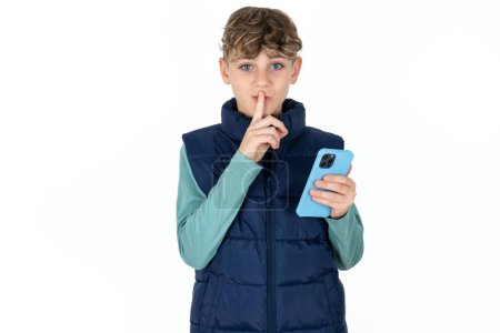 Téléchargez les photos : Beau caucasien adolescent garçon dans bleu gilet tenant moderne gadget demander ne pas dire secrets - en image libre de droit