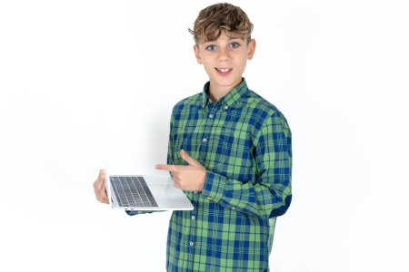 Foto de Shocked guapo adolescente chico usando camisa a cuadros sobre fondo blanco apuntando dedo moderno dispositivo - Imagen libre de derechos