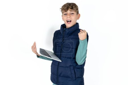 Foto de Guapo caucásico adolescente chico en azul chaleco hold computadora abierto boca levantarse puño - Imagen libre de derechos