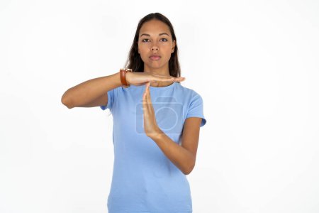 Foto de Joven hermosa mujer hispana vistiendo camiseta azul sobre fondo blanco siendo molesto mostrando un gesto de tiempo de espera, necesita parar, pide tiempo para descansar después del trabajo duro, - Imagen libre de derechos