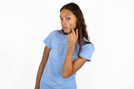 Téléchargez les photos : Jeune belle hispanique femme portant bleu t-shirt sur fond blanc pointant vers l'oeil vous regarder geste, expression suspecte. - en image libre de droit