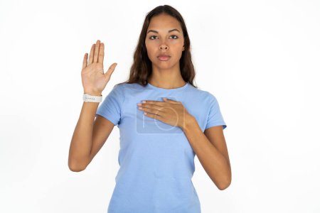 Photo for Young beautiful hispanic woman wearing blue t-shirt over white background Swearing with hand on chest and open palm, making a loyalty promise oath - Royalty Free Image