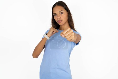 Photo for Young beautiful hispanic woman wearing blue t-shirt over white background Punching fist to fight, aggressive and angry attack, threat and violence - Royalty Free Image
