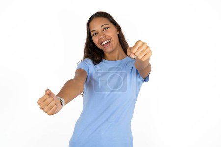 Photo for Young beautiful hispanic woman wearing blue t-shirt over white background imagine steering wheel helm rudder passing driving exam good mood fast speed - Royalty Free Image