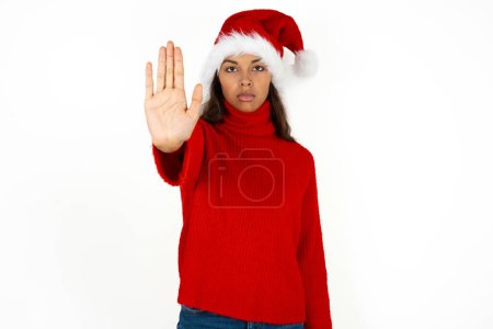 Photo for Young beautiful woman wearing red sweater and santa claus hat at christmas doing stop sing with palm of the hand. Warning expression with negative and serious gesture on the face. - Royalty Free Image