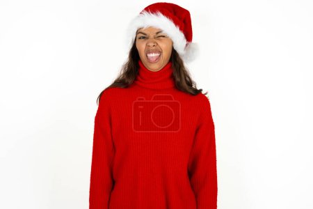 Photo for Young beautiful woman wearing red sweater and santa claus hat at christmas sticking tongue out happy with funny expression. Emotion concept. - Royalty Free Image