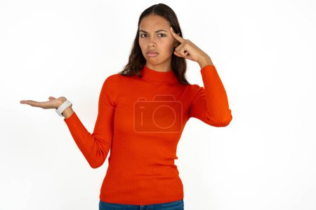 Téléchargez les photos : Jeune femme hispanique portant col roulé rouge sur fond blanc confus et agacé avec la paume ouverte montrant l'espace de copie et pointant du doigt vers le front. Penses-y.. - en image libre de droit