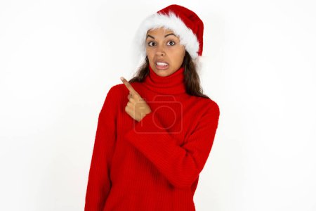 Photo for Young beautiful woman wearing red sweater and santa claus hat at christmas Pointing aside worried and nervous with forefinger, concern and surprise concept. - Royalty Free Image