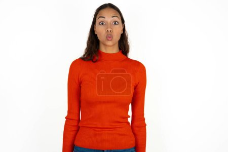 Photo for Shot of pleasant looking young hispanic woman wearing red turtleneck over white background pouts lips, looks at camera, Human facial expressions - Royalty Free Image