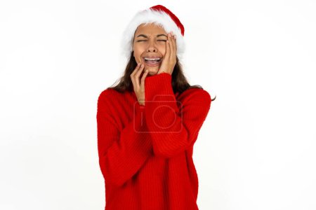 Photo for Doleful desperate crying young beautiful woman wearing red sweater and santa claus hat at christmas looks stressfully, frowns face, feels lonely and anxious - Royalty Free Image