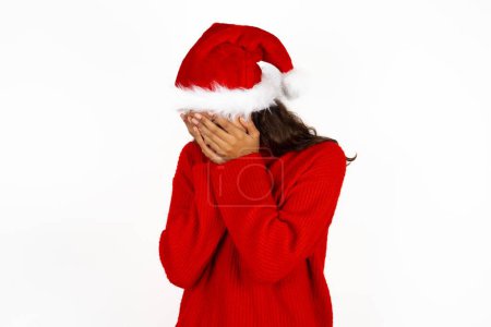 Photo for Sad young beautiful woman wearing red sweater and santa claus hat at christmas crying covering her face with her hands. - Royalty Free Image