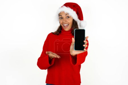 Photo for Young beautiful woman wearing red sweater and santa claus hat at christmas with a mobile. presenting smartphone. Advertisement concept. - Royalty Free Image
