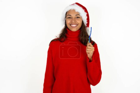 Photo for Young beautiful woman wearing red sweater and santa claus hat at christmas holding a toothbrush and smiling. Dental healthcare concept. - Royalty Free Image