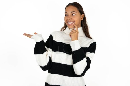 Foto de Positivo joven hermosa mujer con suéter a rayas sobre fondo blanco anuncio promo toque dientes de dedo - Imagen libre de derechos