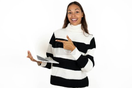 Foto de Sorprendido joven hermosa mujer con suéter a rayas sobre fondo blanco apuntando dedo dispositivo moderno - Imagen libre de derechos