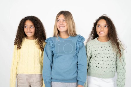 Photo for Amazed Three young beautiful multiracial kid girls biting lip and looking tricky to empty space. - Royalty Free Image