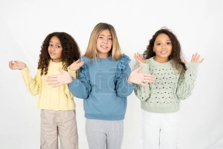Photo for Clueless Three young beautiful multiracial kid girls shrugs shoulders with hesitation, faces doubtful situation, spreads palms, Hard decision - Royalty Free Image