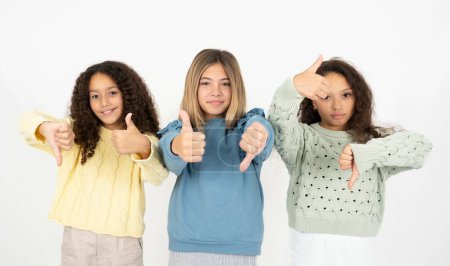 Three young beautiful multiracial kid girls showing thumbs up and thumbs down, difficult choose concept