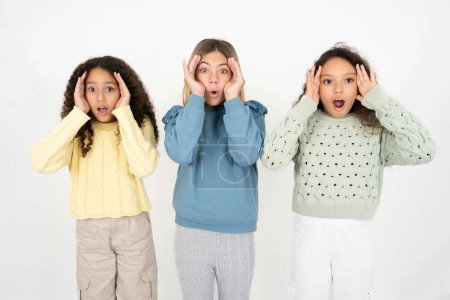 Photo for Three young beautiful multiracial kid girls with scared expression, keeps hands on head, jaw dropped, has terrific expression. Omg concept - Royalty Free Image