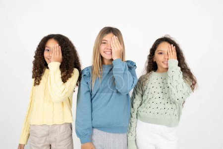 Téléchargez les photos : Trois jeunes belles filles multiraciales couvrant un oeil avec sa main, sourire confiant sur le visage et l'émotion surprise. - en image libre de droit