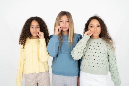 Foto de Tres jóvenes hermosas niñas multirraciales boca y labios cerrados como cremallera con los dedos. Secreto y silencioso, tabú hablando. - Imagen libre de derechos