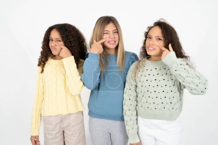 Three young beautiful multiracial kid girls pointing unhappy to pimple on forehead, ugly infection of blackhead. Acne and skin problem