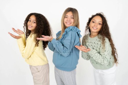 Foto de Tres jóvenes hermosas niñas multirraciales señalando a un lado con las manos abiertas palmeras mostrando espacio de copia, presentando anuncio sonriente emocionado feliz - Imagen libre de derechos